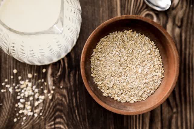Bowl of rolled oats beside a jug of oat milk